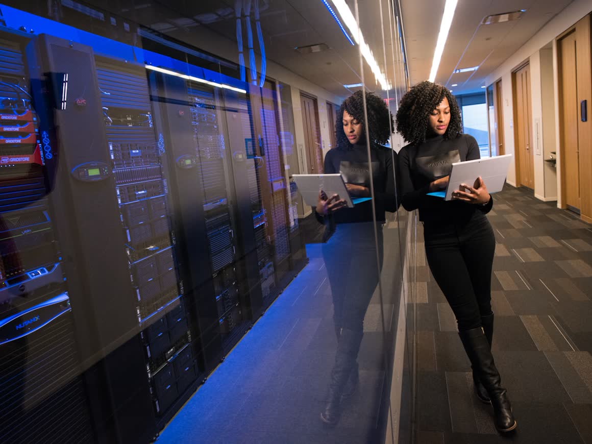 An engineer reviewing systems on a laptop in a blue-lit server aisle